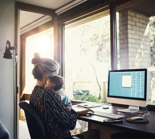 Young mother working on her computer at home with baby on shoulder