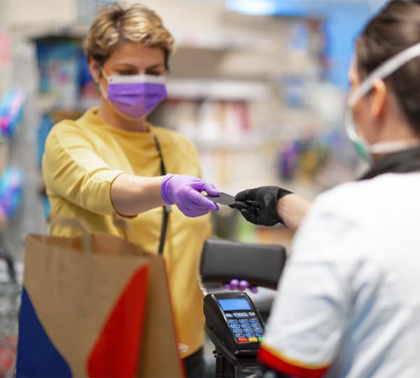 Store cashier returning credit card to woman wearing medical mask and gloves